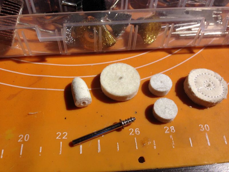 Różne tarcze polerskie z filcu i materiału obok uchwytu na pomarańczowej macie.