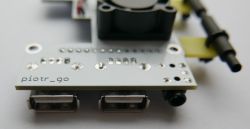 Zbliżenie na płytkę drukowaną z dwoma portami USB i zamontowanym wentylatorem.