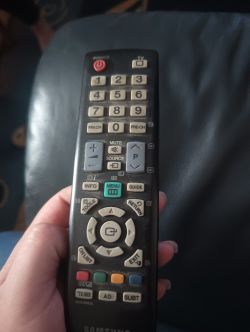 Osoba trzyma pilot Samsung, na którym widać różnorodne przyciski do obsługi telewizora.