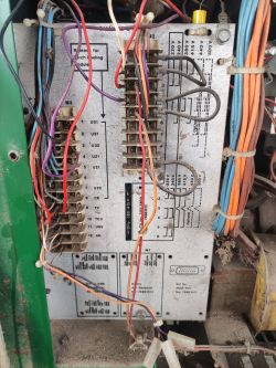 Zbliżenie na tablicę elektryczną z kolorowymi przewodami i listwami zaciskowymi, na tle znajdują się oznaczenia i schematy.