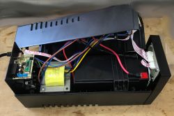 Inside an open UPS case showing battery, transformer, wiring, and small circuit board