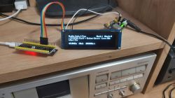 Prototype electronic display on a wooden shelf, showing radio station information.