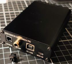 Tył czarnego DAC-a USB z gniazdami Optical, SPDIF, PC USB i Micro USB, na macie z siatką.