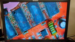 Zdjęcie monitora Lenovo wyświetlającego zbliżenie układu elektronicznego z elementami takimi jak kondensatory, cewki i układy scalone.