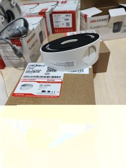 Biały uchwyt montażowy Hikvision na pudełku, w tle opakowania kamer Turbo HD