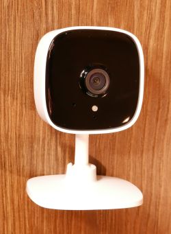 Kamera TP-Link Tapo C100 zamontowana na białej podstawie na tle drewnianej ściany