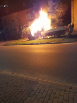 Samochód dostawczy w płomieniach zaparkowany na trawie przy budynku mieszkalnym nocą
