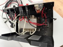 Widok wnętrza urządzenia elektronicznego z plątaniną przewodów, w tym widocznym czarnym przewodem do podłączenia.