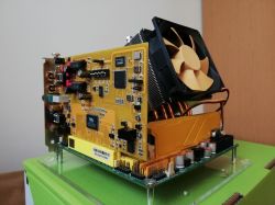 Expansion card with yellow PCB and a large fan on a heatsink, mounted on a clear standoff base