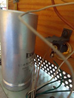 Duży aluminiowy kondensator z przewodami wewnątrz obudowy urządzenia elektronicznego.