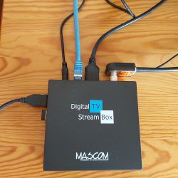 Mascom Digital TV Stream Box tuner connected to various cables on a wooden table.