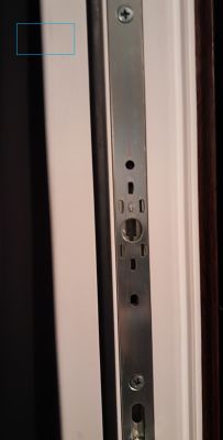 Metalowy mechanizm zasuwnicy okiennej zamocowany na białej ramie z dwoma widocznymi śrubami.