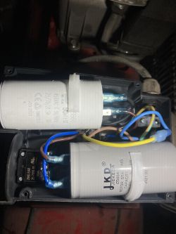 Widok wnętrza obudowy sprężarki z kondensatorami i przewodami elektrycznymi.