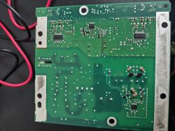 Zielona płytka PCB z elementami SMD i ścieżkami, widok od spodu; po bokach metalowe płytki i przewody.