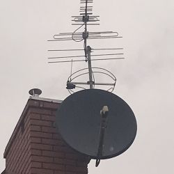 Talerz anteny satelitarnej i antena naziemna zamontowane na kominie budynku
