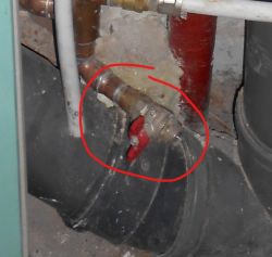 Zawór spustowy z czerwoną dźwignią na instalacji rurowej, zaznaczony czerwonym okręgiem