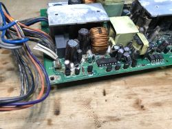 Fragment zdemontowanego zasilacza z płytą PCB, elementami elektronicznymi i pękiem przewodów.
