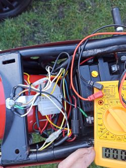 Zbliżenie na instalację elektryczną motocykla z widocznymi przewodami i multimetrem.