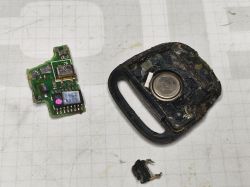 Stary, uszkodzony pilot samochodowy, częściowo rozłożony z widocznymi elementami elektronicznymi.