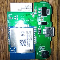 Close-up of a PCB with WBRG1 module, micro‑USB port, and a push button on a wooden surface