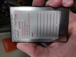 Karta PCMCIA z napisem ostrzegawczym i liniami do notatek trzymana w ręce.