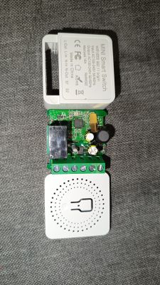 Disassembled mini Wi-Fi smart switch with visible PCB on fabric background.