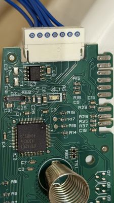 Close-up of a PCB with ICs, a white connector, blue wires, and a metal coil spring