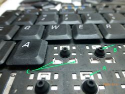 Zbliżenie na rozebraną klawiaturę laptopa z wyjętymi przyciskami i zaznaczonymi elementami mechanizmu za pomocą liter A, B, C.