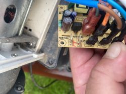 Zbliżenie na płytkę elektroniki z kondensatorami i przewodami, trzymaną w dłoni przy obudowie urządzenia