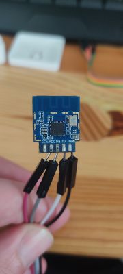 A blue electronic module with connected wires, held in hand, on a wooden table background.