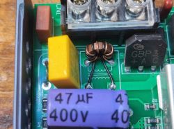 Zbliżenie PCB z kondensatorem 47 µF 400V, dławikiem i mostkiem GBP3 obok złącz śrubowych.