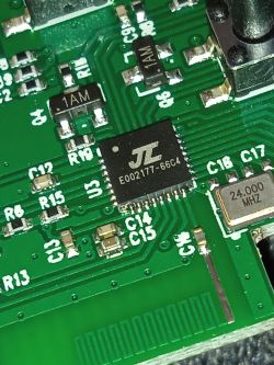 Makrofotografia zielonej płytki PCB z układem JL E002177-66C4 i rezonatorem 24.000 MHz
