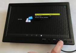 Small black monitor showing OSD menu; a finger presses a button on the lower control panel.