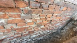 Odsłonięty fundament z czerwonej cegły z widocznymi ubytkami w spoinach.