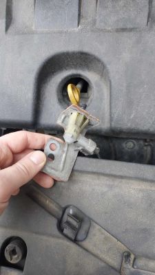 Osoba trzyma metalowy uchwyt z plastikowym elementem przed komorą silnika samochodu.