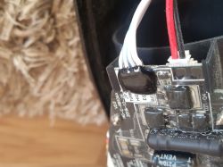 Zbliżenie płytki elektroniki z przewodami w złączach, z czarną masą zalewową na elementach.