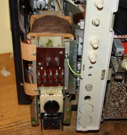 Wnętrze starego urządzenia elektronicznego z widocznym transformatorem, pokrętłami i przewodami.