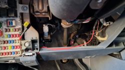 Widok na wnętrze skrzynki bezpiecznikowej samochodu z dodatkowym czerwonym kablem.