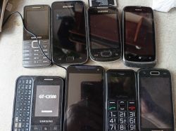 Kilka staromodnych telefonów różnych marek, z których tylko jeden jest włączony, podłączony do ładowarki.