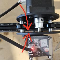 Czerwone strzałki wskazujące na poluzowaną śrubkę w mechanizmie laserowym