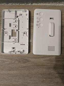 The image shows two parts of a plastic intercom casing lying on a wooden surface.