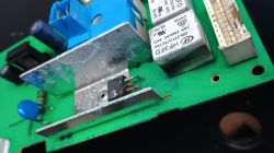Uszkodzony tranzystor na zielonej płytce PCB z widocznym radiatorem i innymi podzespołami elektronicznymi.