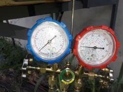 Dwa manometry: niebieski i czerwony, zamontowane na mosiężnym rozdzielaczu.
