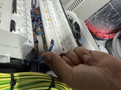 Osoba trzyma przewód o odsłoniętym, niezaizolowanym końcu przy rozdzielnicy elektrycznej z zamontowanymi rozłącznikami.