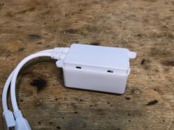 LED Strip Controller on Wooden Surface Small white plastic box with cables on a wooden surface.