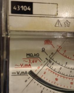 Skala analogowego miernika z podziałkami i oznaczeniami.