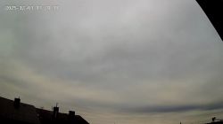 Camera snapshot showing rooftops and cloudy sky with date and time overlay in the corner