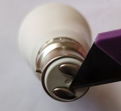 A GU10 light bulb socket with metal contacts and a purple knife blade pointing at the contacts.
