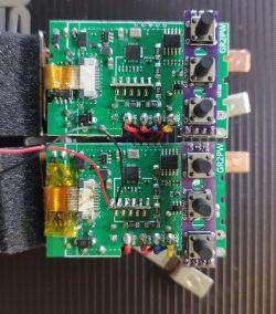Two identical electronic modules, one above the other, showing PCBs, buttons, and colored wires.
