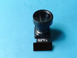 Miniature SP0828 V1.0 camera module with lens Miniature camera module on a blue background, with a large lens and 0828 V1.0 marking on the board.
